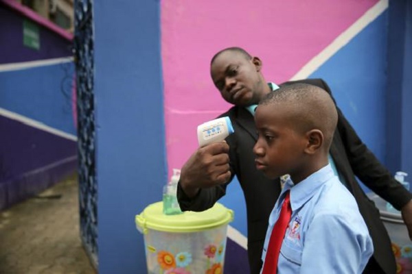 A school official takes a pupil's temperature using an infrared digital laser thermometer in front of the school premises, at the resumption of private schools, in Lagos
