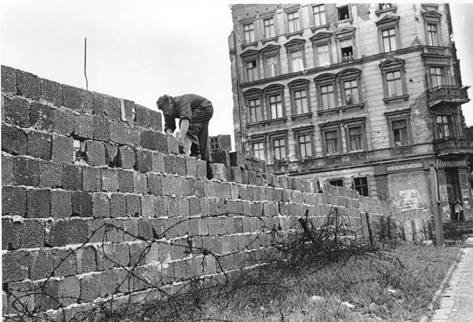 An East Berlin policeman puts bricks in place as the Berlin Wall is heightened to 15 feet, 5 m, separating East and West Berlin, Germany, on Sept. 9, 1961.  People watch from their apartment building windows in background above. (AP Photo)