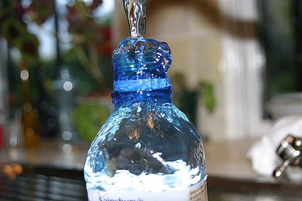 Tap water filling and overflowing a mineral water bottle.