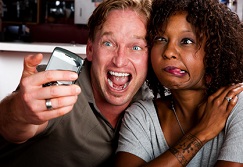 Caucasian man and African American woman taking picture in coffee house with cell phone