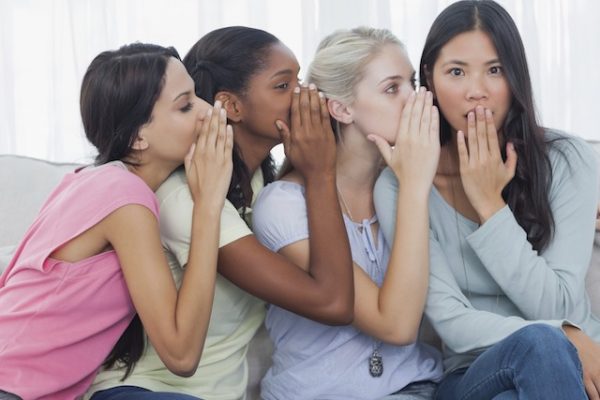 Friends whispering secret to shocked brunette
